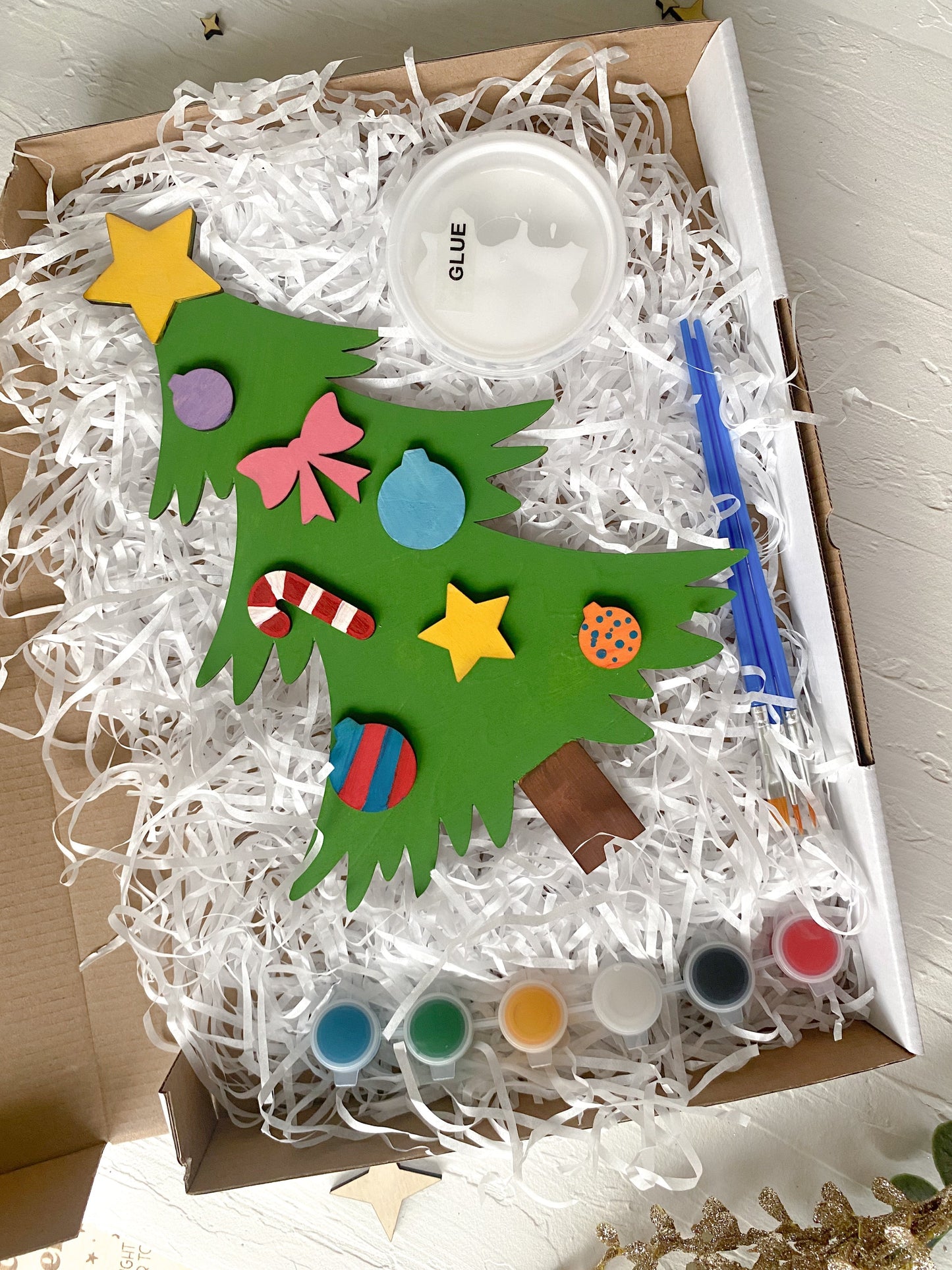 A Christmas Tree DIY Kit with various colors of paint, paintbrushes, and decorative attachments, displayed in an open box.