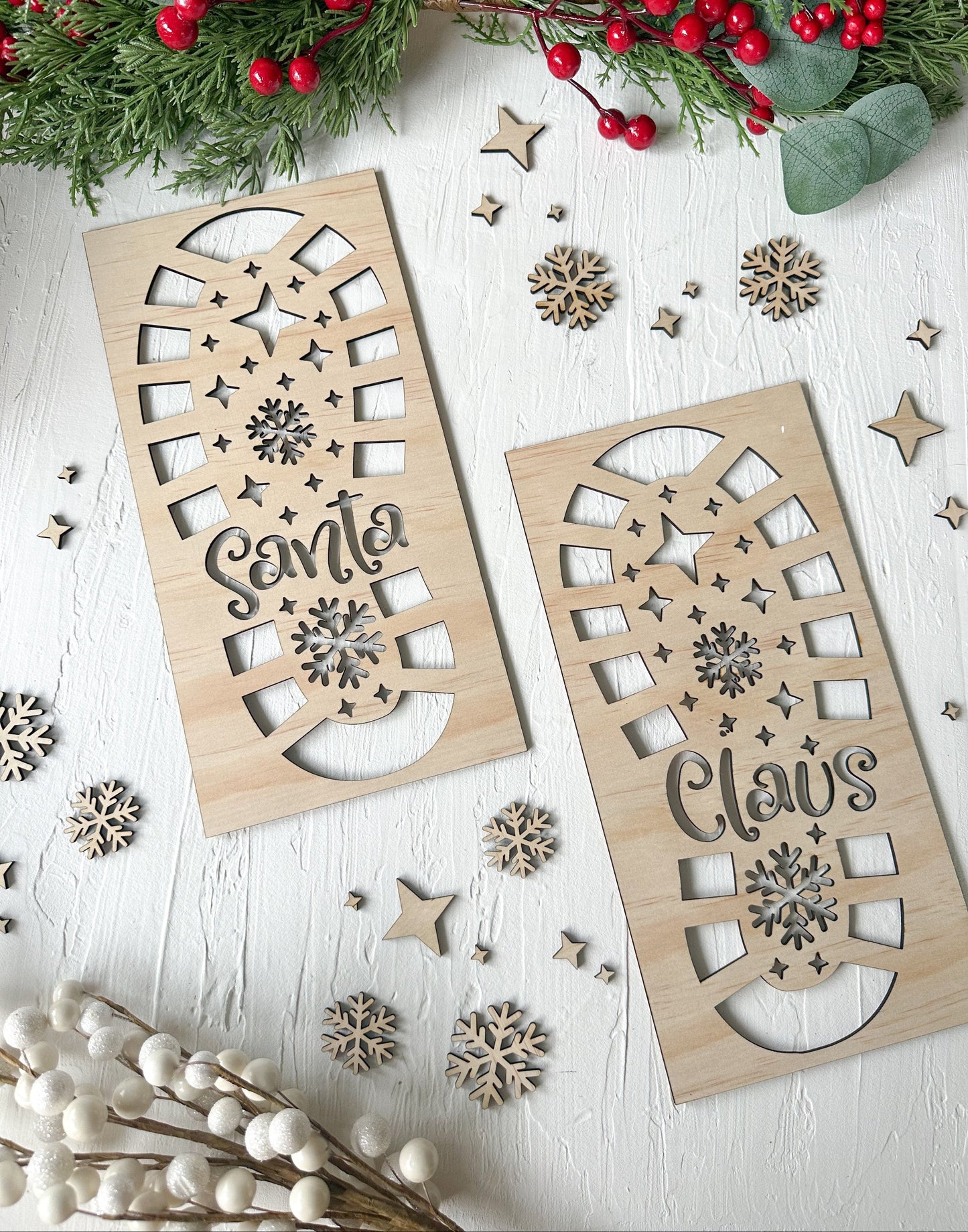 Two wooden stencils designed to create footprints resembling Santa's boots, surrounded by festive decorations like pine cones, berries, and artificial snow.